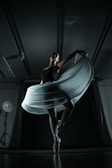 A ballerina gracefully balances on pointe, her elegant pose emphasized by a flowing skirt that catches the light. The dimly lit studio showcases dramatic shadows, enhancing the sense of movement and poise.