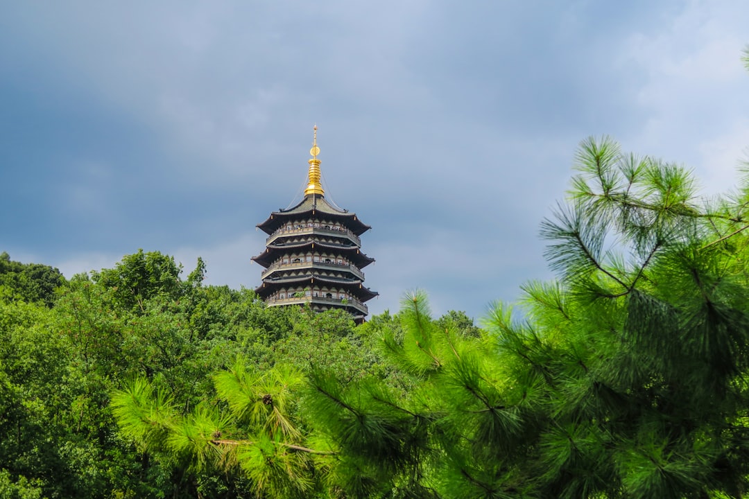 a tall building behind trees with Leifeng Pagoda in the background,