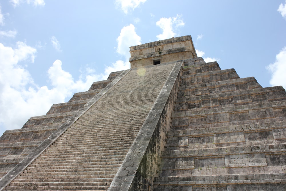 a stone pyramid with a blue sky with Chichen Itza in the background