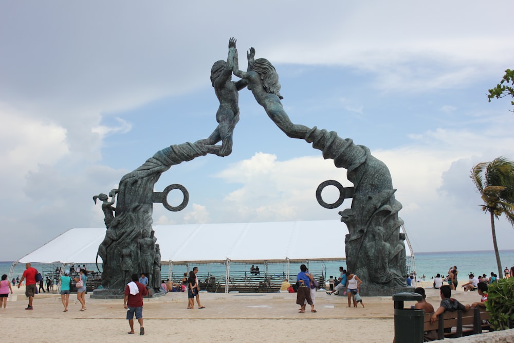 a group of people walking around a statue on a beach