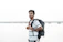 Smiling young Indian man with a backpack, standing by a scenic riverside.