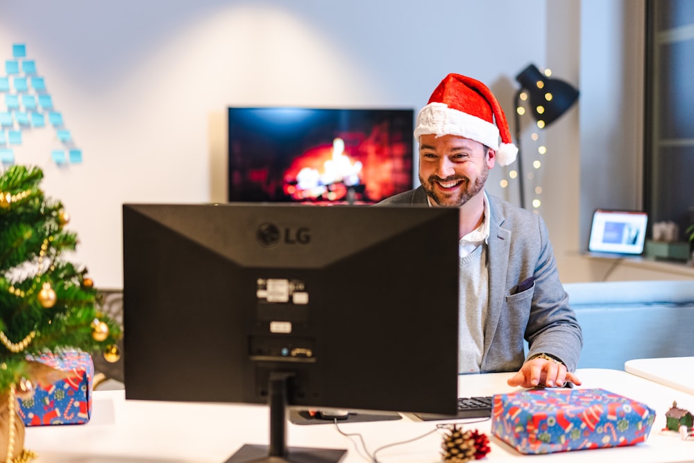 a man wearing a santa hat and sitting at a computer