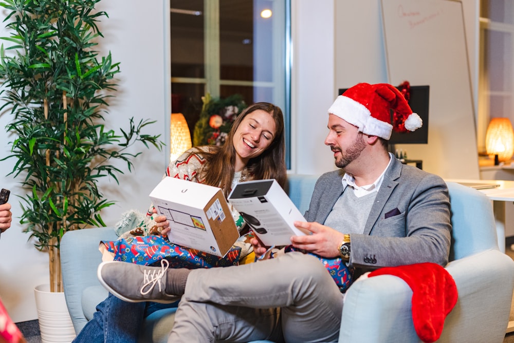 a man and woman sitting on a couch with a christmas hat and a book