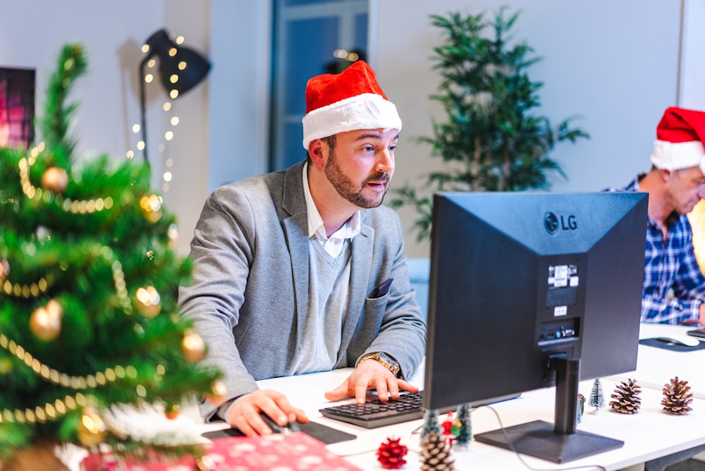 a man wearing a santa hat and sitting at a computer