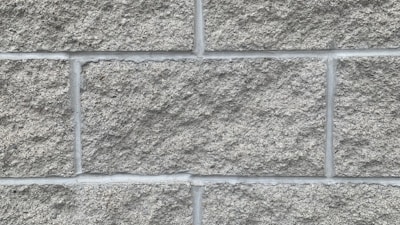 A close-up view of a wall constructed from rough gray concrete blocks arranged in a neat, grid-like pattern. The texture is coarse and slightly uneven, with visible grout lines separating each block.