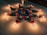 A colorful rangoli design on the floor is surrounded by lit oil lamps. The rangoli features a central blue flower pattern with orange and white circular accents, complemented by green leaf motifs.
