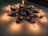 A colorful rangoli design on the floor is surrounded by lit oil lamps. The rangoli features a central blue flower pattern with orange and white circular accents, complemented by green leaf motifs.