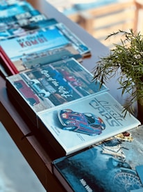 Several books are arranged on a wooden table, with a focus on one titled 'Classic Cars' featuring a colorful car illustration. The scene captures a cozy, well-lit environment with a plant visible on the side.