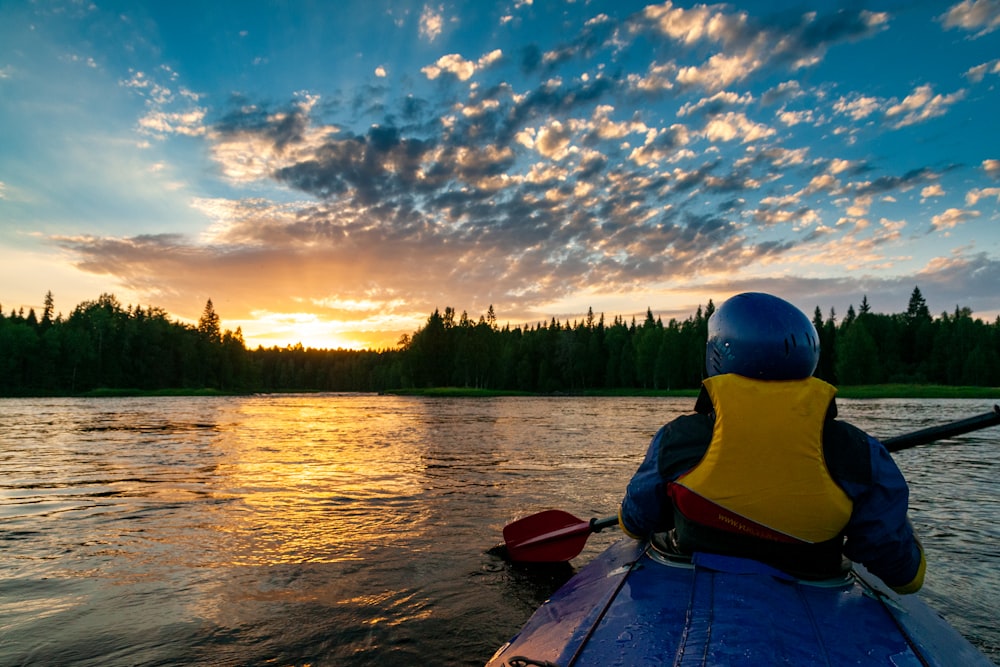 a person in a kayak on a lake with trees and a sunset