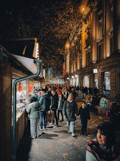Evening scene with warm market lights glowing over a crowd chatting and browsing local goods