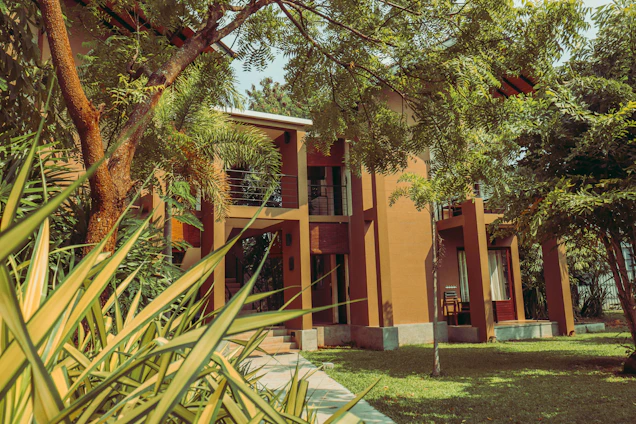 A sunlit exterior shot of Havona Suites showcasing modern architecture with lush greenery surrounding the homestay buildings.
