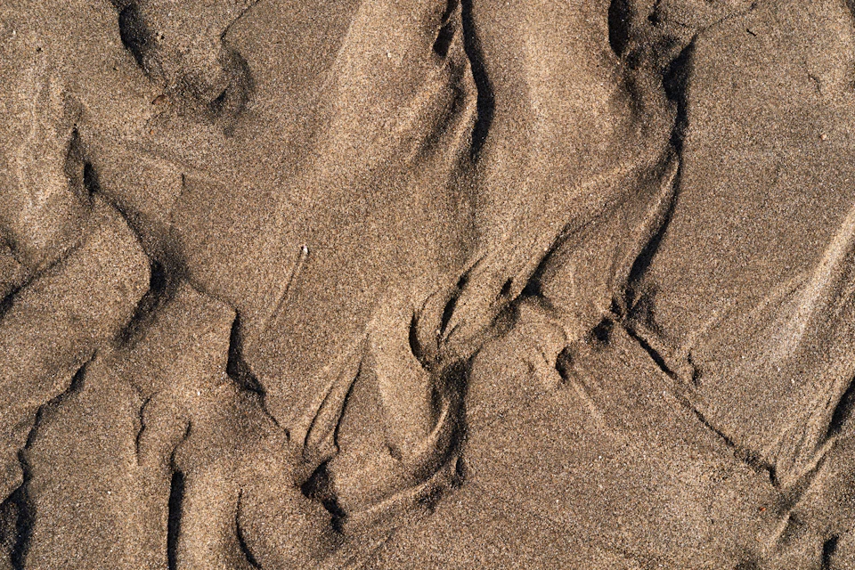 Close-up view of sandy beach with light brown sand and rippled texture created naturally