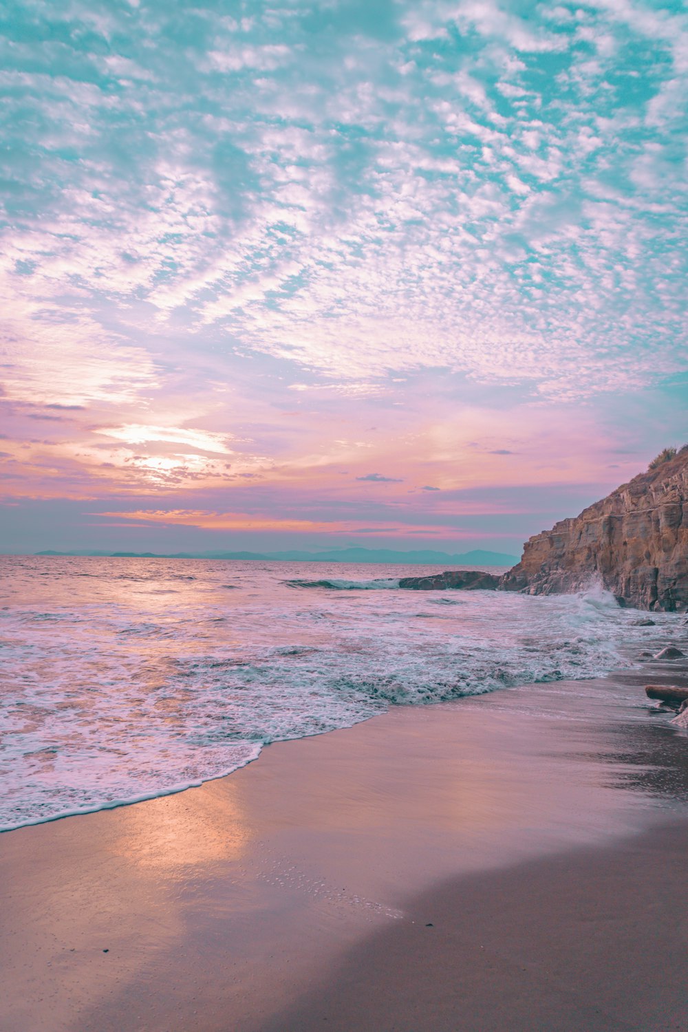 a beach with a rock cliff and water with a blue sky