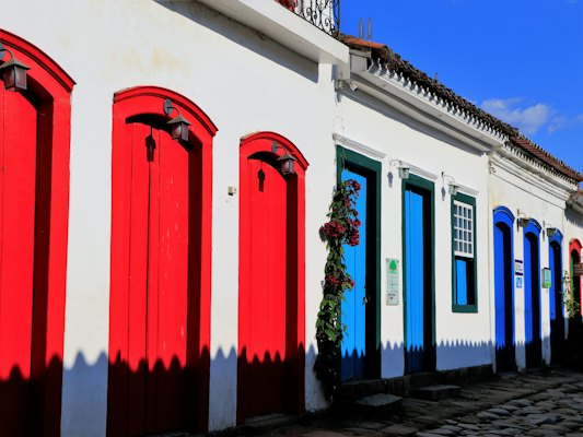 Red and blue doors along a row of whitewashed houses — Paraty, Brazil