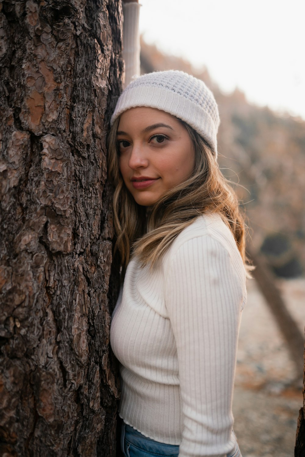 a woman wearing a white hat and standing next to a tree