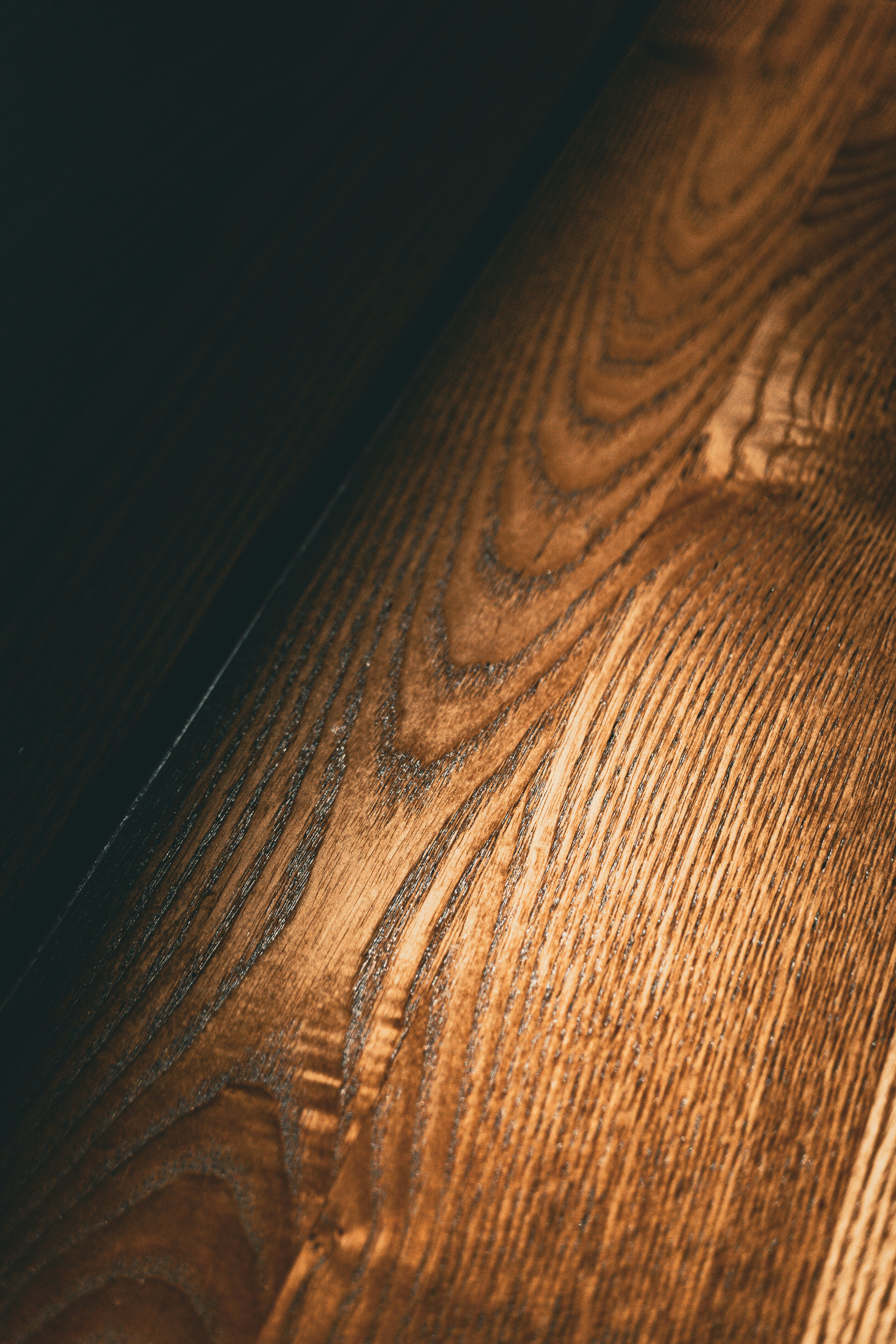 Textura de madera oscura con veta pronunciada, iluminación cálida lateral, superficie pulida con profundidad visual
