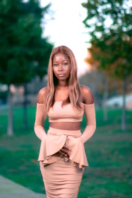 Model wearing a flowing beige dress against a warm, sunlit backdrop.