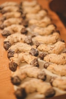 Rows of crescent-shaped cookies are arranged neatly, with a delicate dusting of powdered sugar on top. The cookies have their ends dipped in dark chocolate, creating a visually appealing contrast.