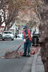 A bright orange leaf blower clearing autumn leaves on a driveway.