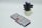 A smartphone displaying an app screen lays on a white surface next to a small potted plant with vibrant purple flowers.