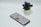 A smartphone displaying an app screen lays on a white surface next to a small potted plant with vibrant purple flowers.