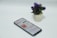 A smartphone displaying an app screen lays on a white surface next to a small potted plant with vibrant purple flowers.