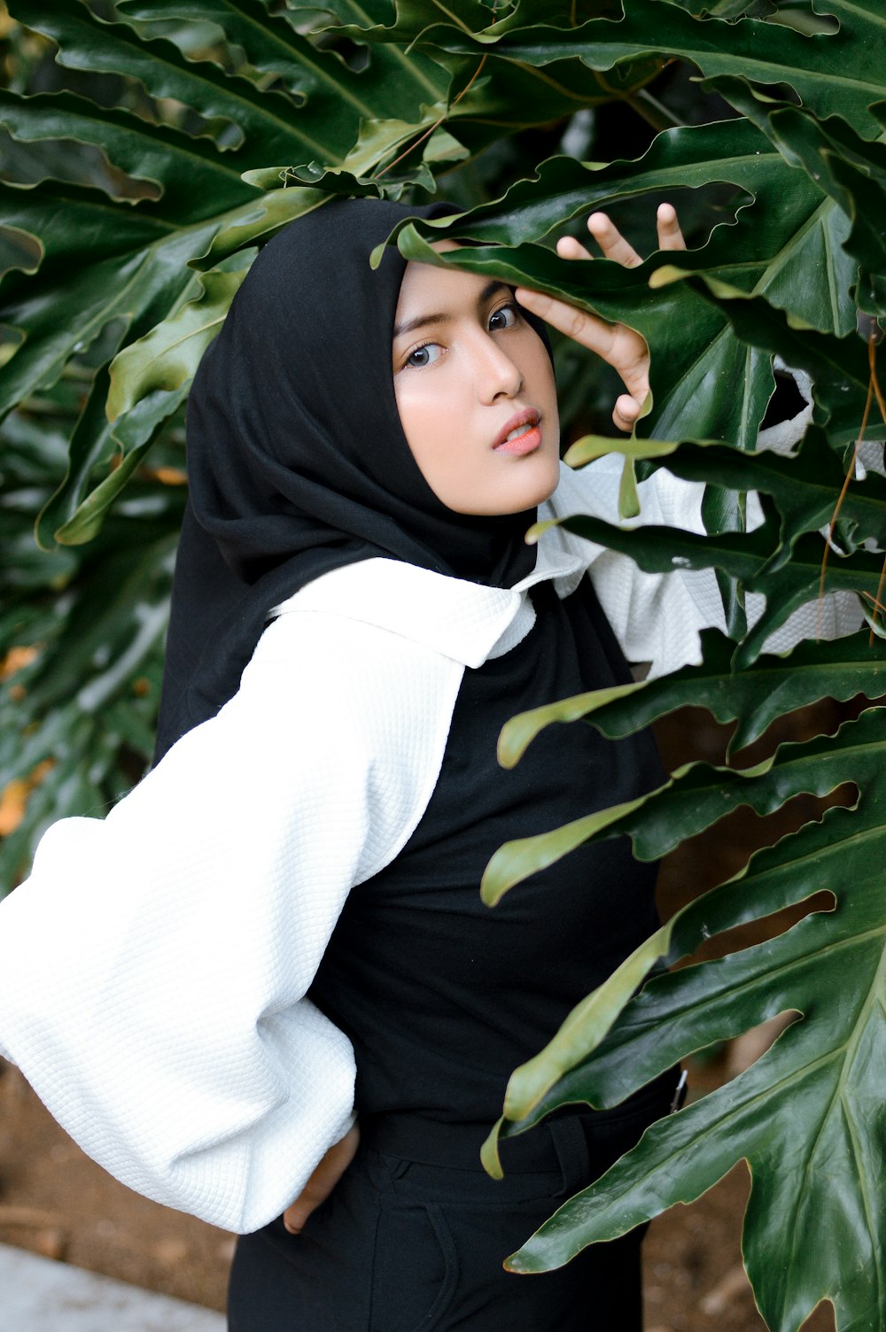 a person in a black head scarf standing in front of a large green plant