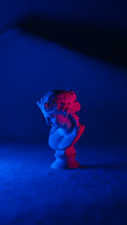 A refined shot of a philosopher’s bust statue bathed in warm light with a backdrop of deep blue drapery.
