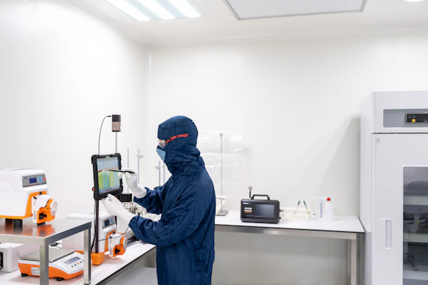 A professional laboratory technician in a sterile cleanroom suit using a tablet to monitor specializ