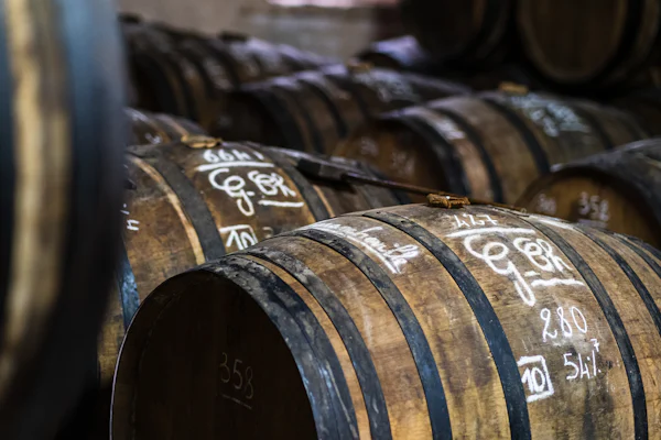 Barricas de roble en una bodega de envejecimiento en primer plano — el corazón de canela, roble y haba tonka de Angels' Share de Kilian Paris, por la perfumería Olara