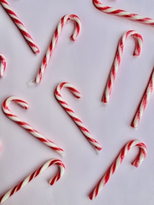 Several red and white striped candy canes are arranged on a light pink background. The candy canes vary in direction and spacing, creating a visually appealing pattern.