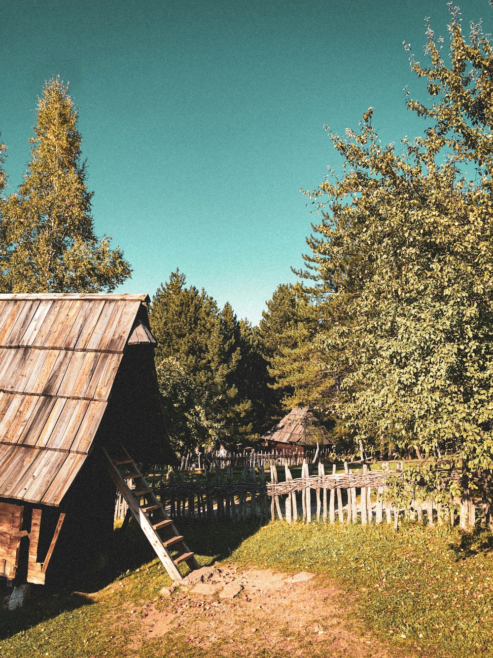 a wooden house with a fence and trees in the background