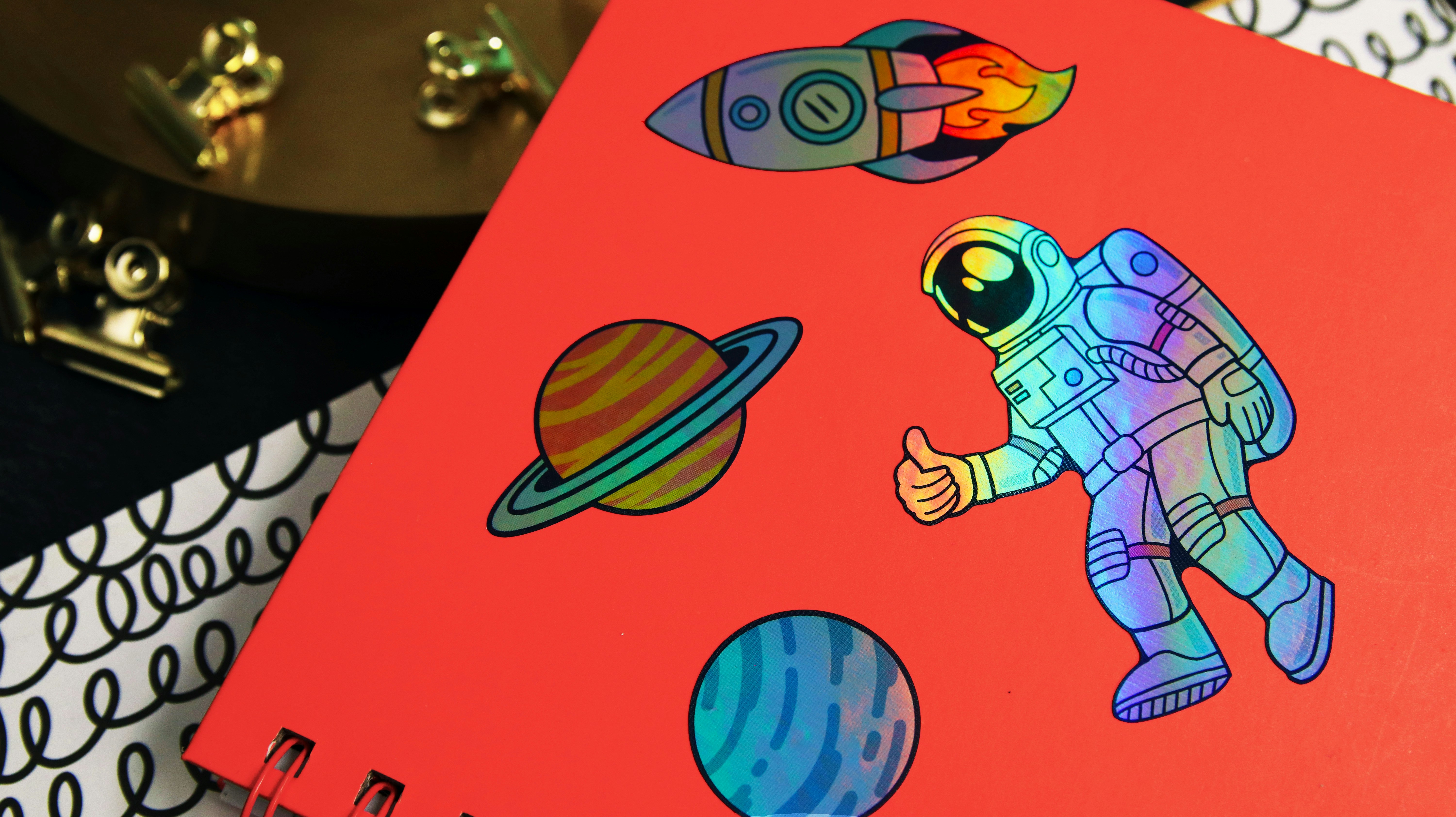 Several holographic die cut stickers with space designs applied to a pink notebook