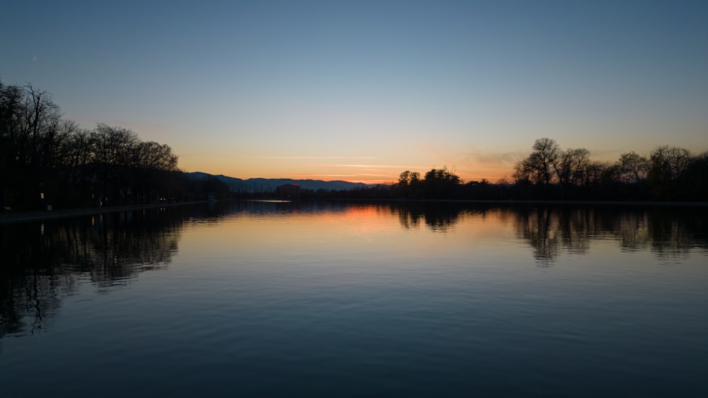 un plan d’eau avec des arbres et un coucher de soleil en arrière-plan