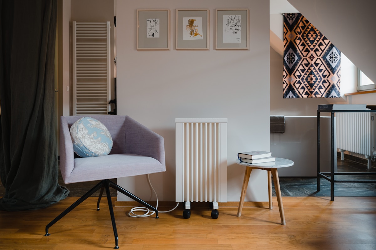 Small apartment reading nook with lavender armchair, row of three small framed prints above, kilim wall hanging and wooden side table