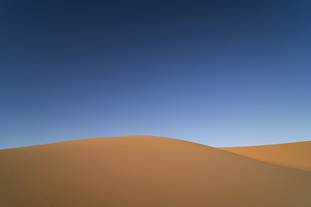 A sand dune under a blue sky photo – Free Nature Image on Unsplash