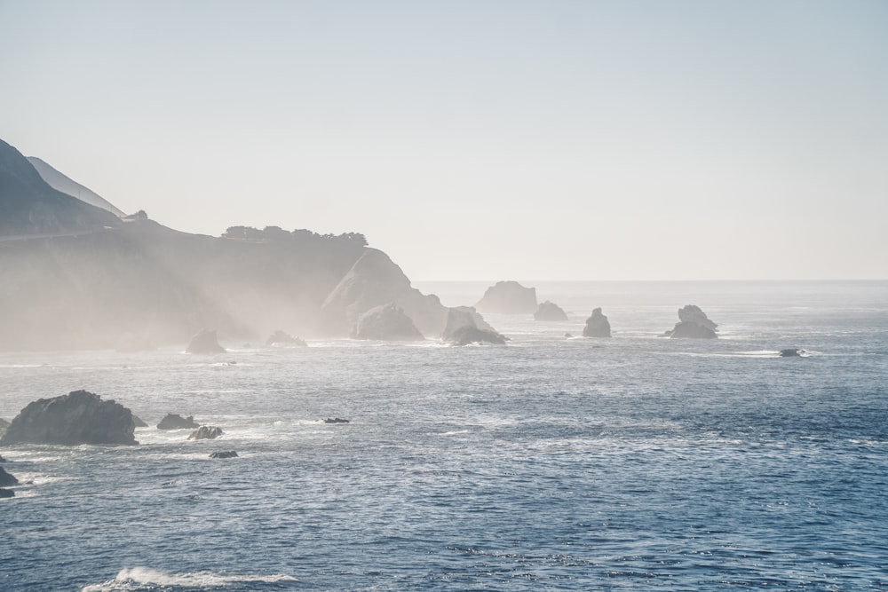 a body of water with rocks in it and fog around it