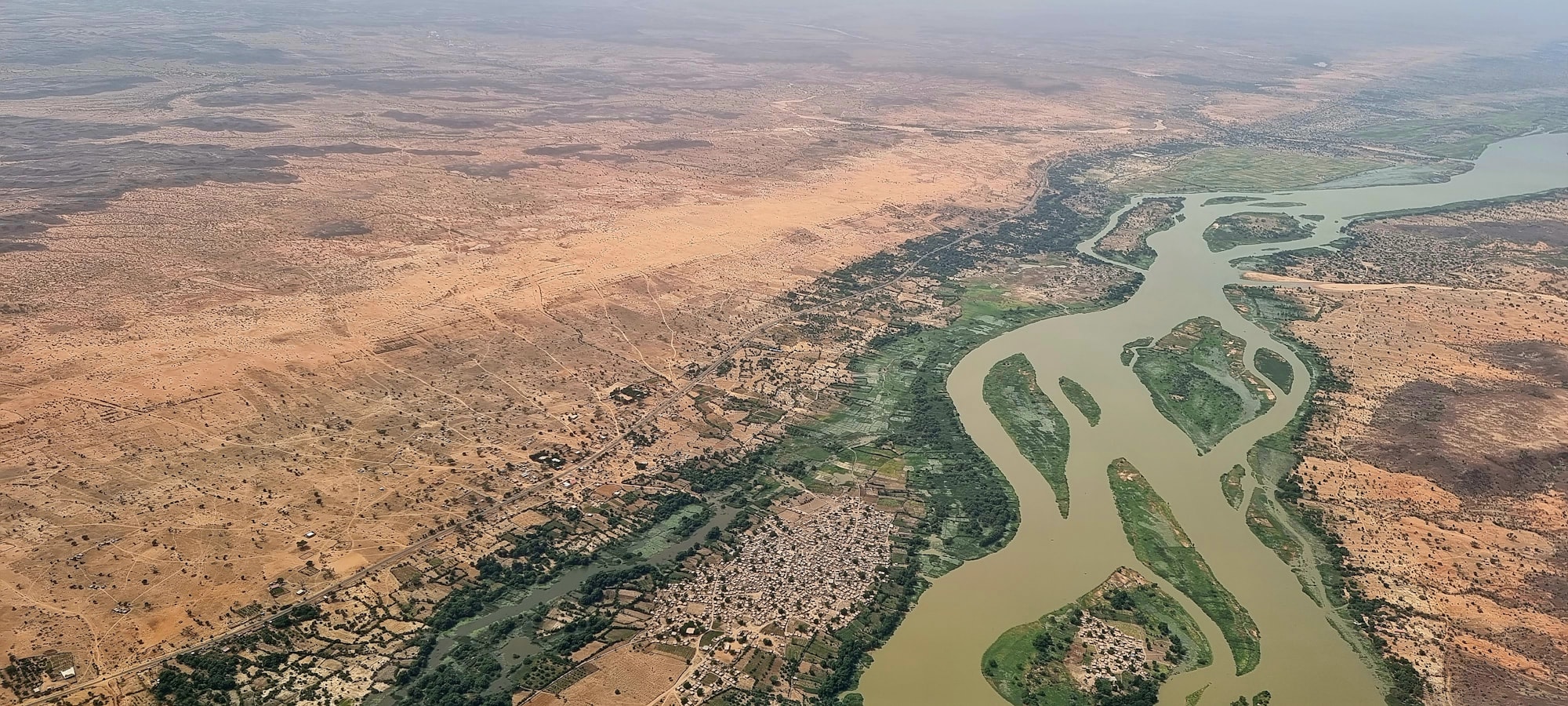 A narrow strip of river in the Sahel, with desert stretching away in the distance.