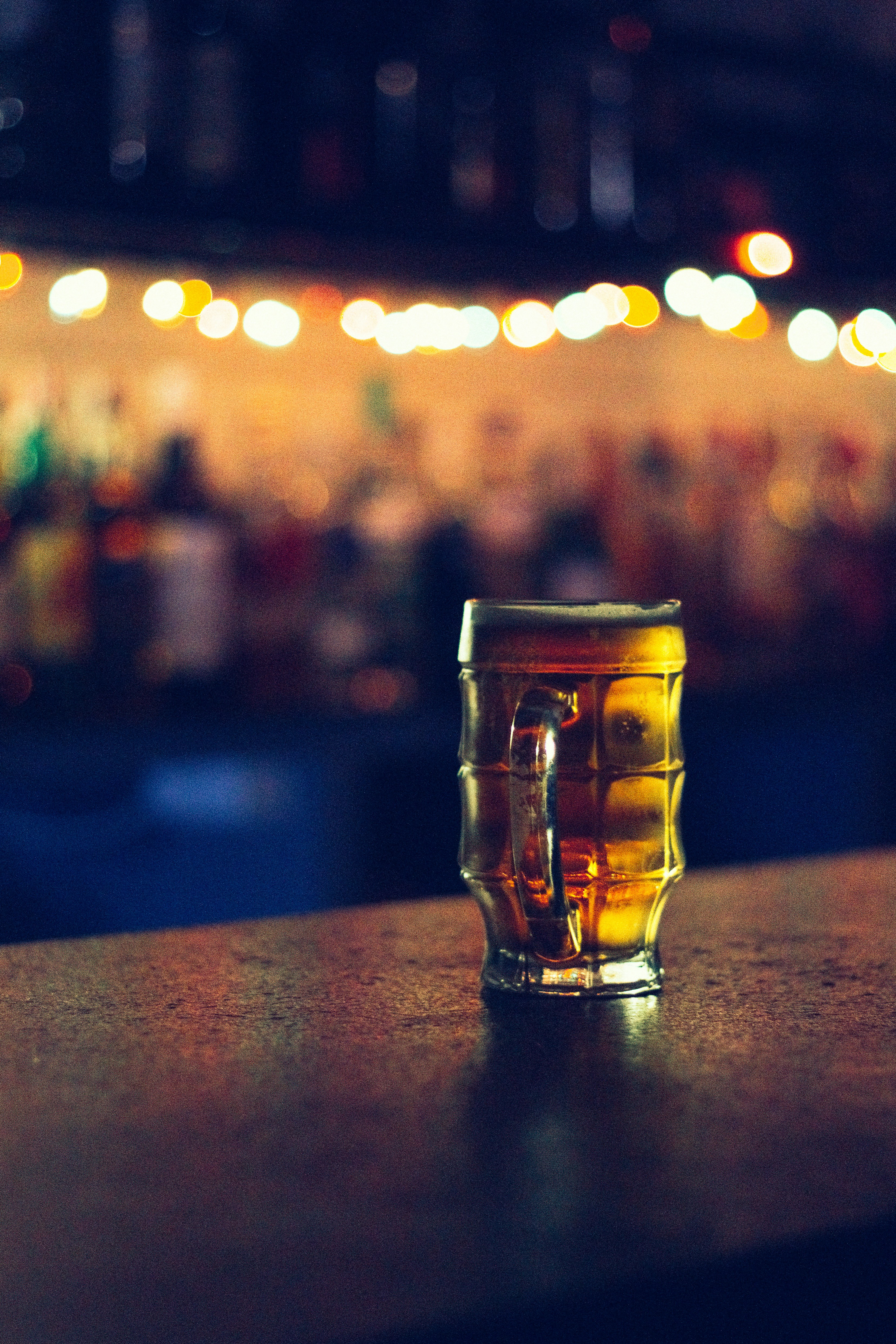 Assorted craft beer bottles and glasses on wooden bar, warm golden lighting