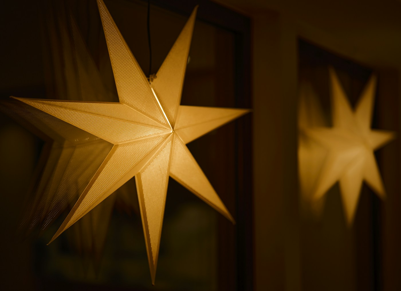 Two warm yellow paper stars glowing in a dark window.