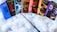A collection of seven books from the Harry Potter series is displayed on a fluffy white surface. Each book has a colorful and distinct cover design. A wand is placed in front of the books, creating a magical theme.