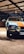 A classic car parked indoors, featuring a distinctive blue and orange paint job. The setting is well-lit with spotlights, and a brick wall is visible in the background. The car's headlights are prominent, and the area exudes a vintage aesthetic.
