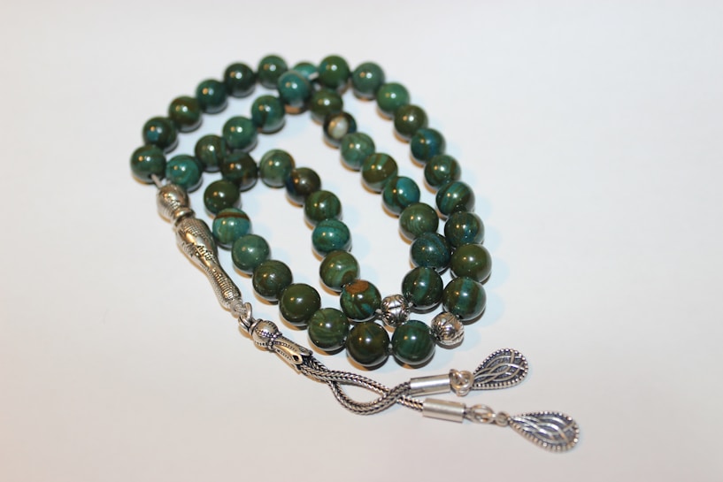 A strand of prayer beads with polished green stones, intricately designed silver separators, and decorative metallic tassels.