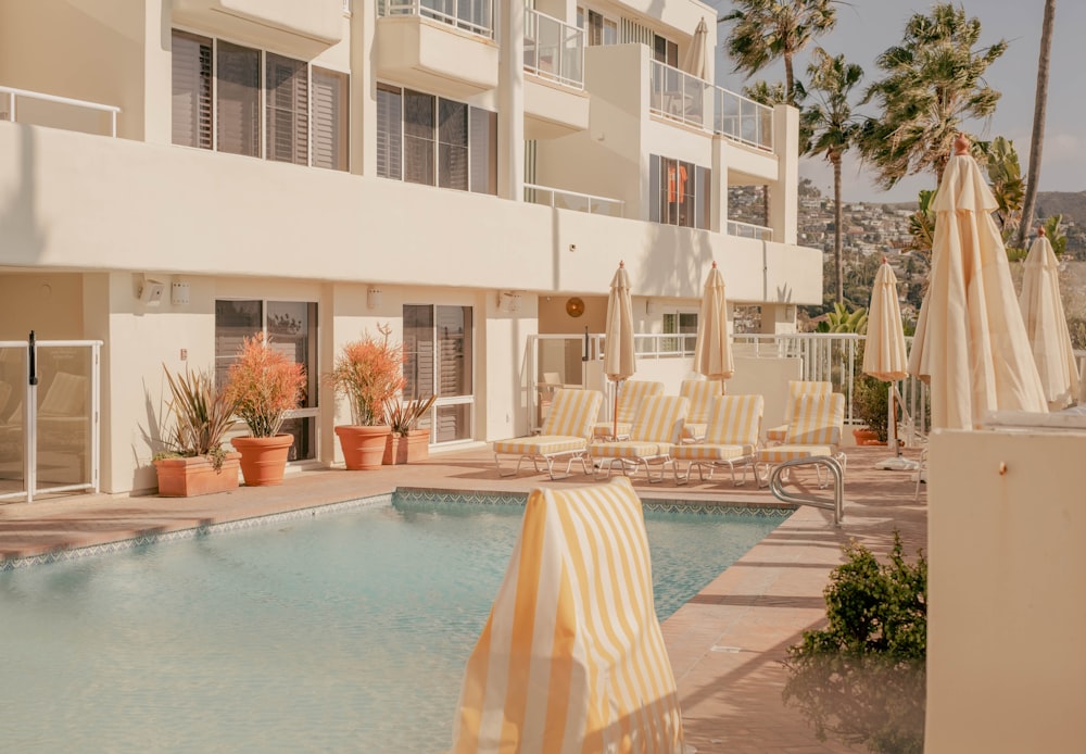 a swimming pool with chairs and umbrellas next to a building