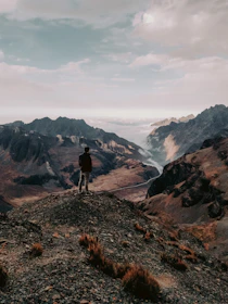 A cinematic frame of a traveler standing on a mountain peak, overlooking misty valleys at dawn.