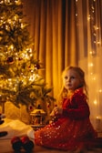 a girl sitting next to a christmas tree
