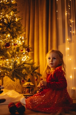 a girl sitting next to a christmas tree