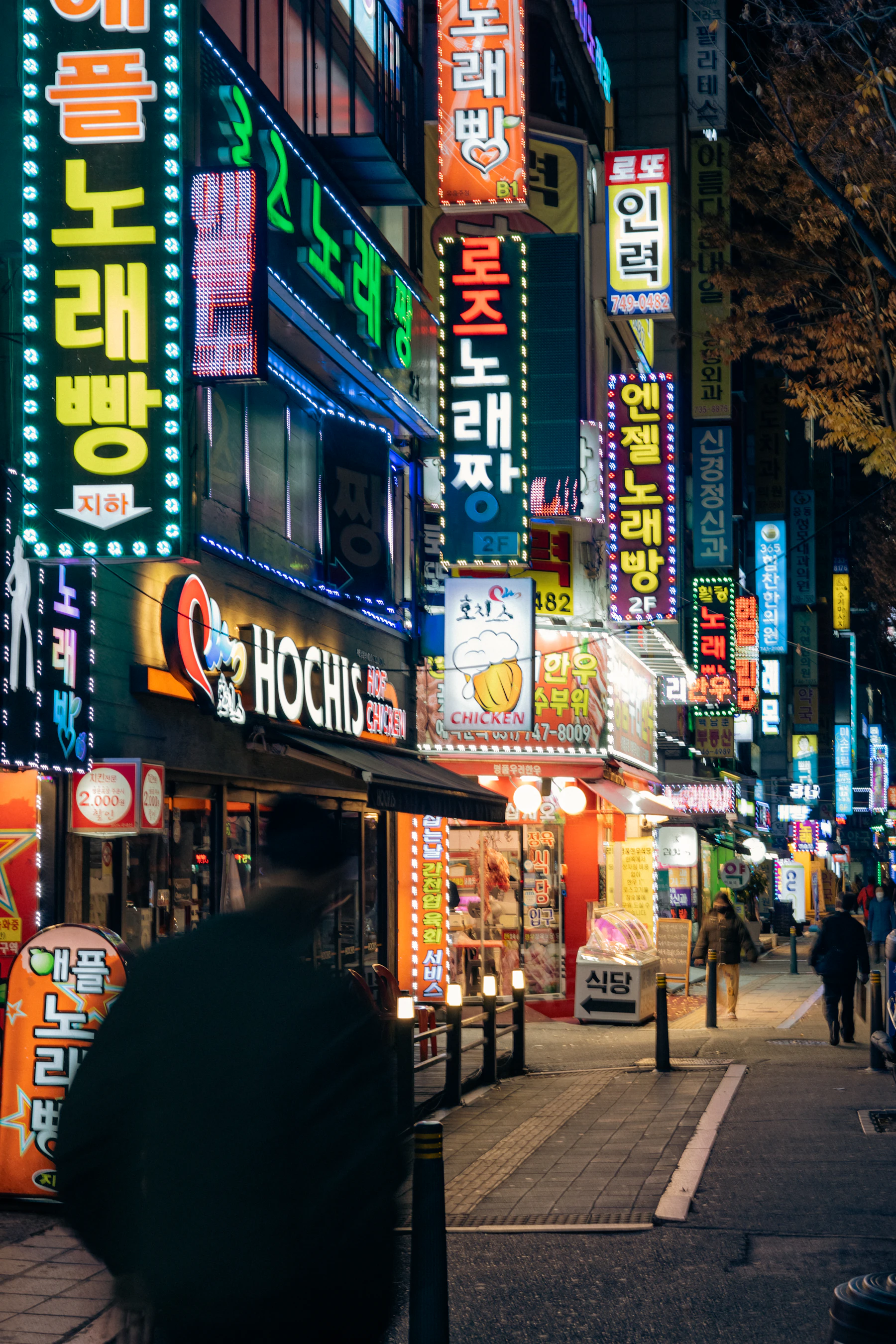 A Seoul side street at night, both sides stacked with glowing neon shop signs in Hangul