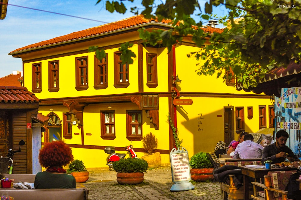 a yellow building with a few people sitting at tables