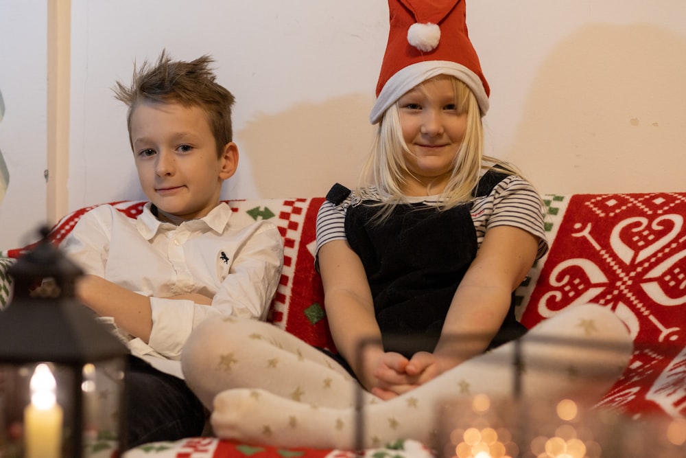 a boy and girl sitting on a couch with a santa hat